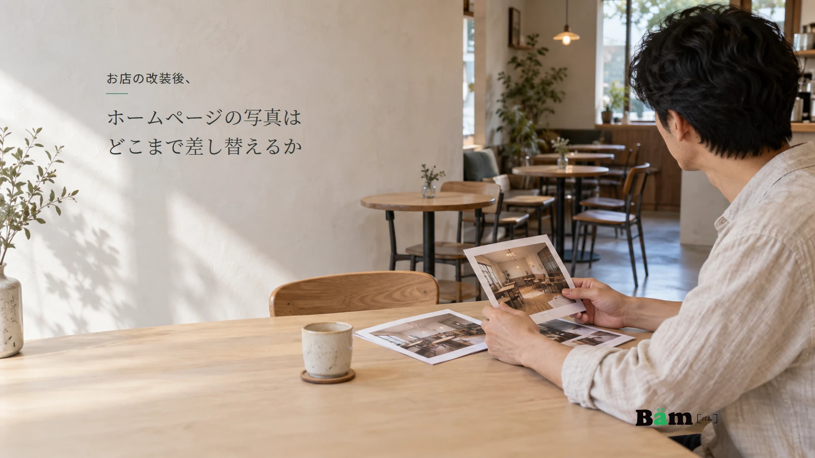 改装後のカフェで、店主が店内の写真と現在の席の配置を見比べている様子。