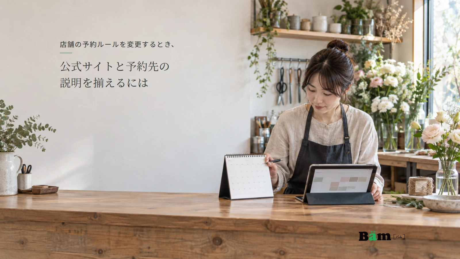 花のワークショップの店頭で、カレンダーと予約画面を確認する店主の説明用写真。全文タイトルと正式Bämロゴを配置。