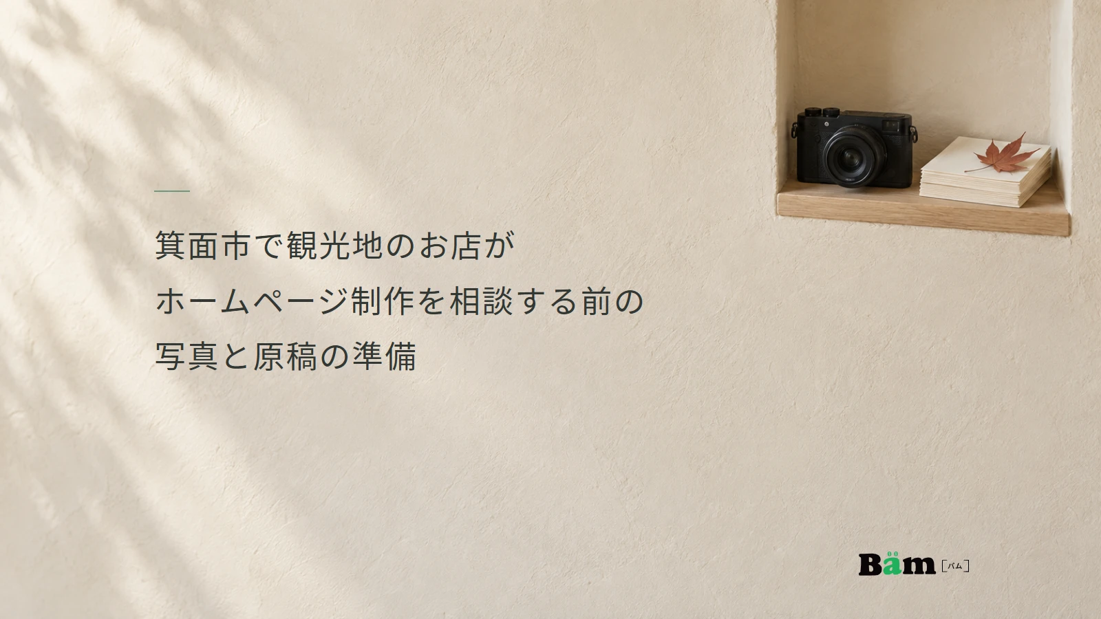 箕面市で観光地のお店がホームページ制作を相談する前の写真と原稿の準備というタイトル、明るい壁と小さな棚のカメラと紙、右下のBämロゴ