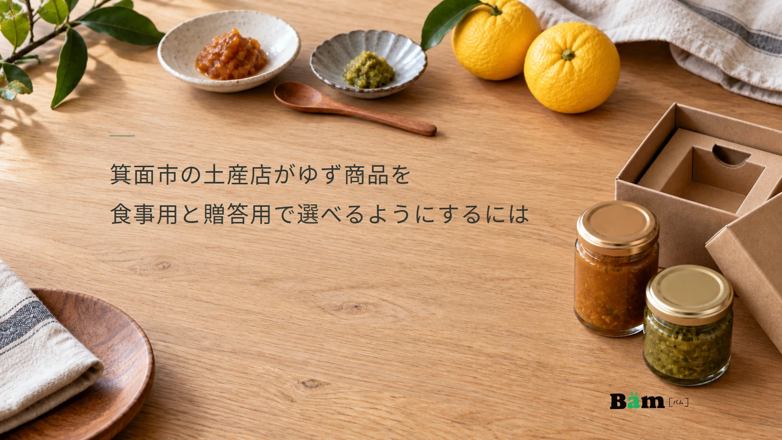 箕面市の土産店がゆず商品を食事用と贈答用で選べるようにするにはというタイトル、二種類のゆず調味料と小皿、贈答箱を並べた木のテーブル、右下にBämロゴ