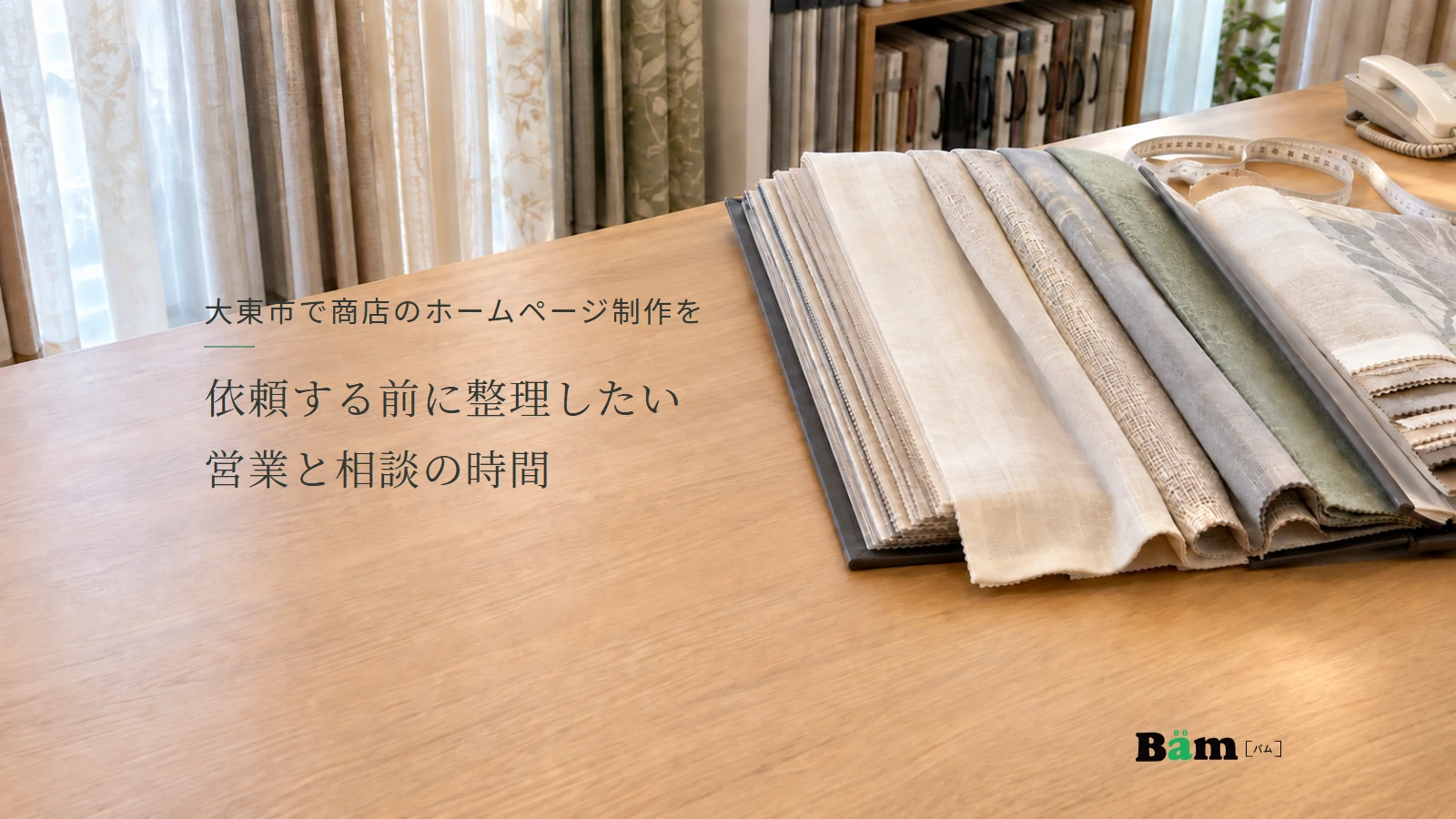 大東市で商店のホームページ制作を依頼する前に整理したい営業と相談の時間というタイトル、カーテン生地の見本帳とメジャー、奥に電話がある相談台、右下にBämロゴ
