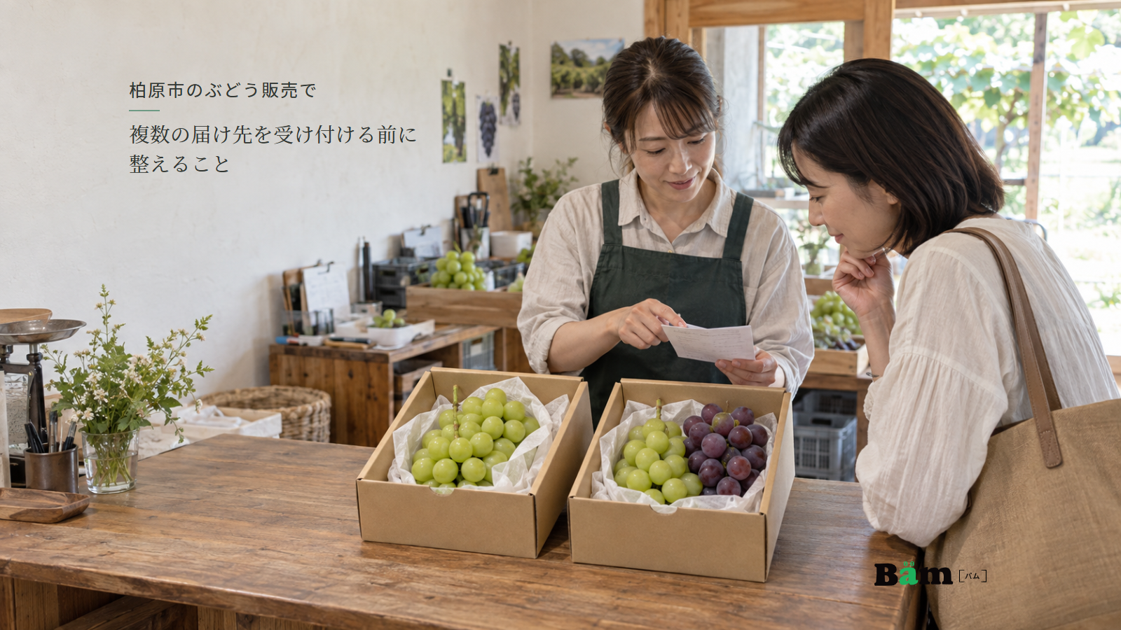 柏原市のぶどう販売で複数の届け先を受け付ける前に整えることという全文タイトル、二種類のぶどうの箱と注文メモを確かめる農園スタッフとお客様、右下のBämロゴ