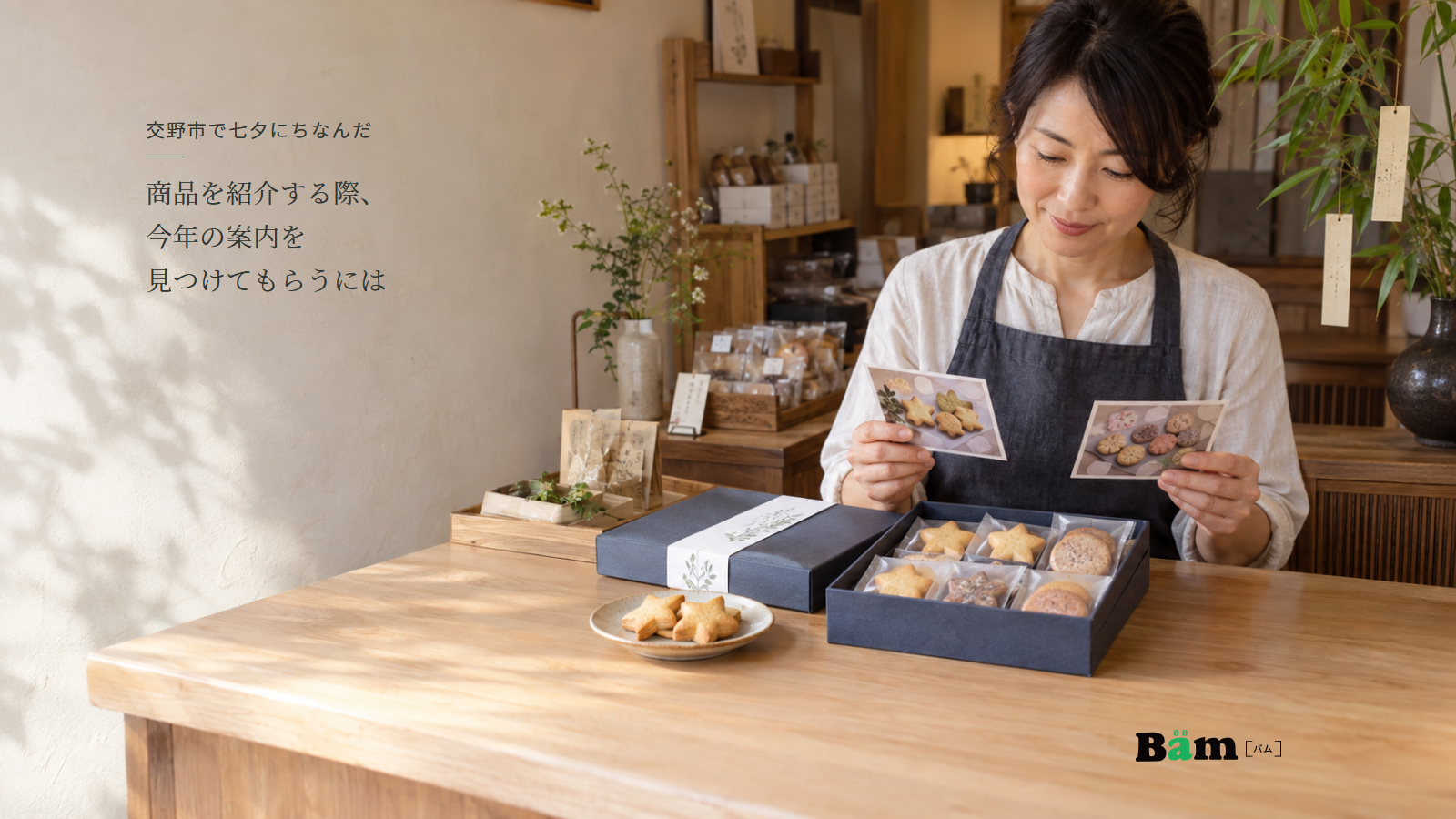 菓子店の木のカウンターで二枚の商品写真を見る女性と星形焼菓子の贈答箱、交野市で七夕にちなんだ商品を紹介する際、今年の案内を見つけてもらうにはの全文タイトル、右下のBämロゴ