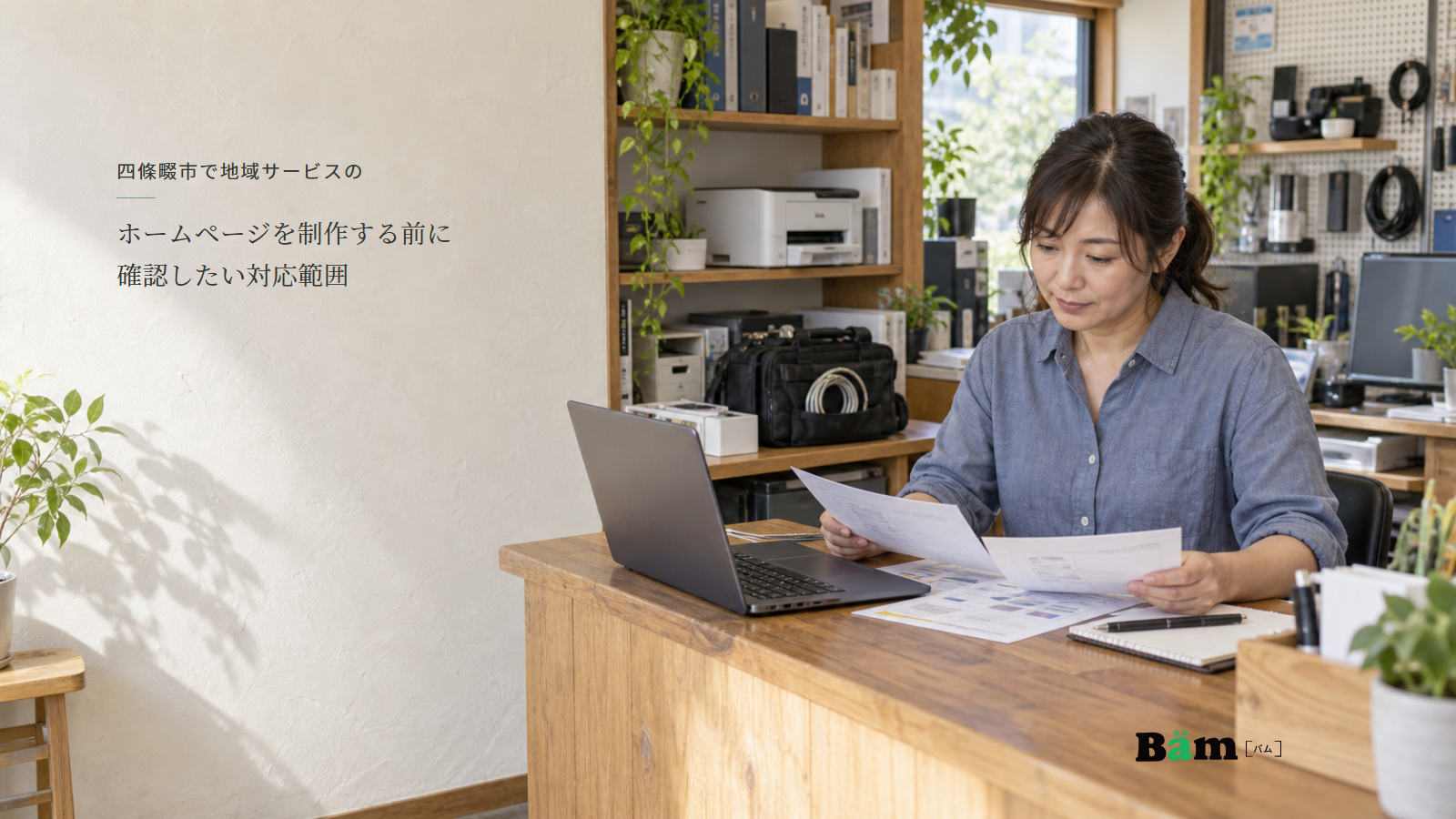 パソコン相談店でノートPCや出張用バッグのそばで案内資料を見比べる店主、四條畷市で地域サービスのホームページを制作する前に確認したい対応範囲の全文タイトル、右下のBämロゴ