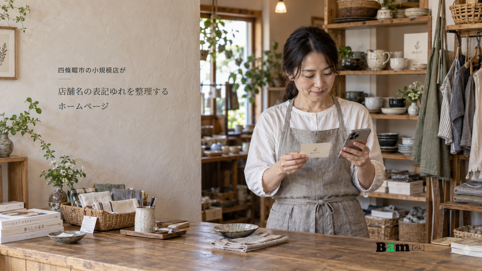 陶器と布小物が並ぶ雑貨店でショップカードとスマートフォンを見比べる店主、四條畷市の小規模店が店舗名の表記ゆれを整理するホームページの全文タイトル、右下のBämロゴ
