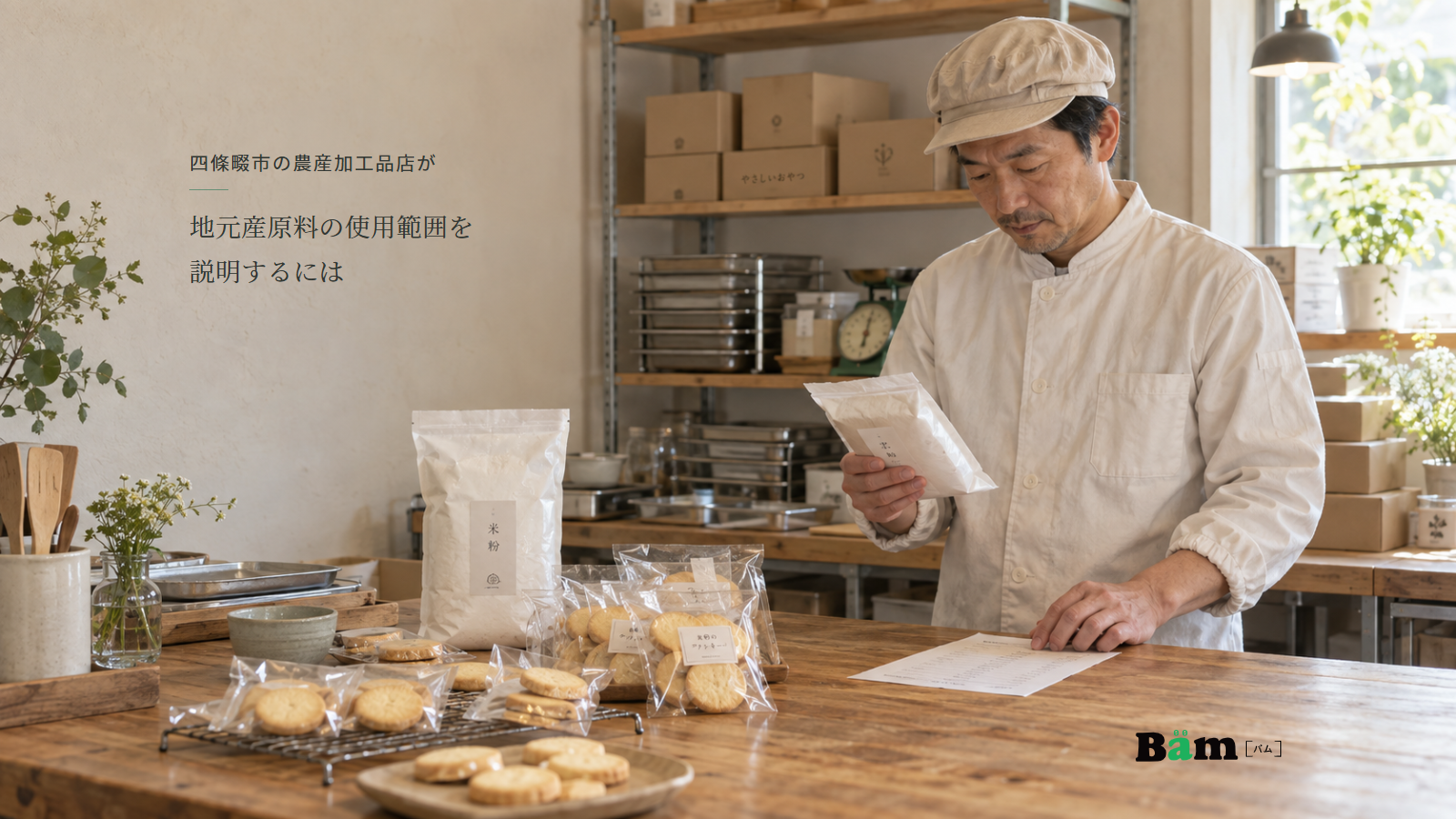 米粉と包装済みクッキーがある菓子店の作業台で原料袋と資料を確認する担当者、四條畷市の農産加工品店が地元産原料の使用範囲を説明するにはの全文タイトル、右下のBämロゴ