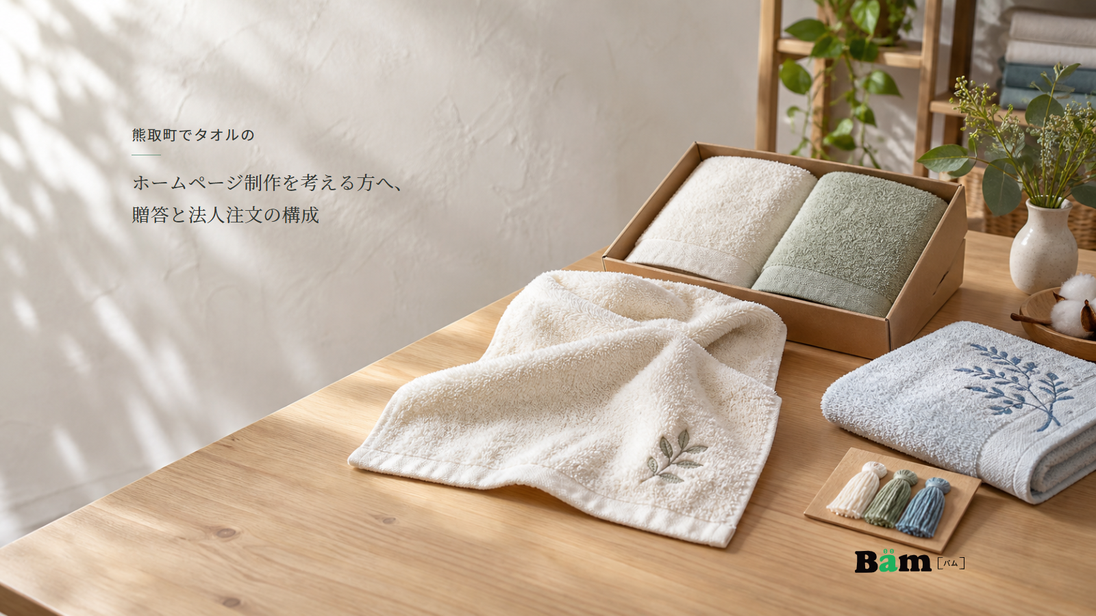 明るいタオル見本机に贈答セット、葉模様の刺繍と印刷の見本、糸見本が並ぶ場面、熊取町でタオルのホームページ制作を考える方へ、贈答と法人注文の構成の全文タイトル、右下のBämロゴ