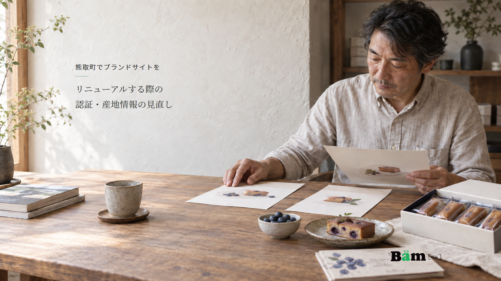 焼菓子とブルーベリーを置いた机で、店主が複数の商品資料を見比べる場面、熊取町でブランドサイトをリニューアルする際の認証・産地情報の見直しの全文タイトル、右下のBämロゴ