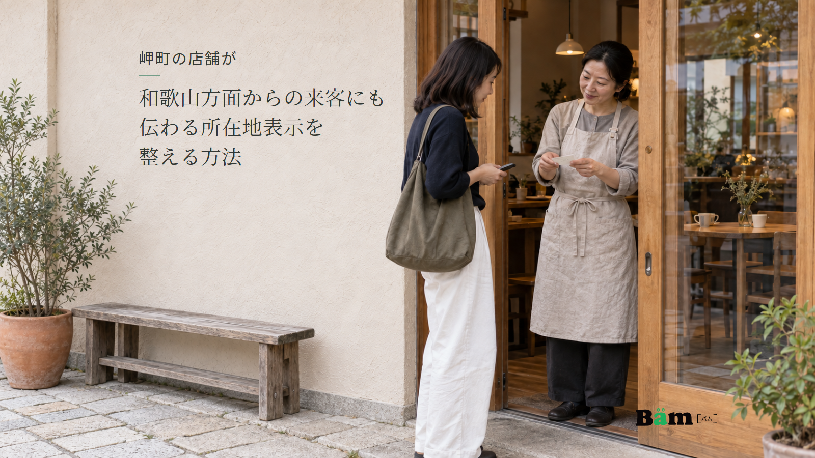 カフェの入口で店主が案内カードを持ち、スマートフォンを手にした来客へ説明する場面、岬町の店舗が和歌山方面からの来客にも伝わる所在地表示を整える方法の全文タイトル、右下のBämロゴ
