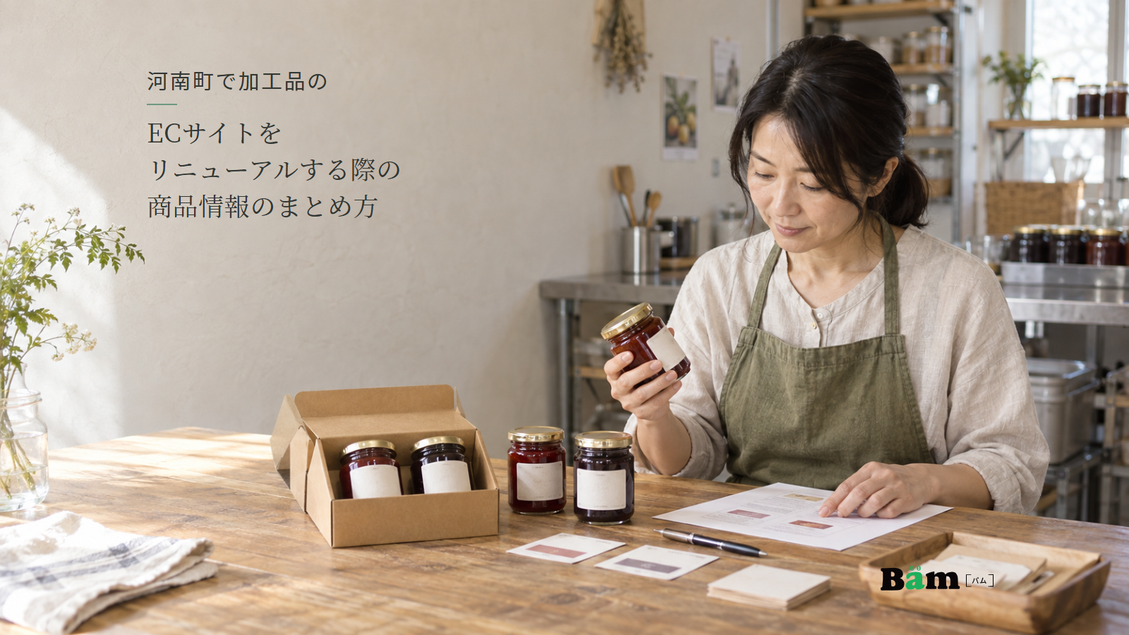 果実加工の工房で女性がジャム瓶と資料を照合し、机に単品の瓶と二瓶入りの箱、ラベル見本が並ぶ場面、河南町で加工品のECサイトをリニューアルする際の商品情報のまとめ方の全文タイトル、右下のBämロゴ