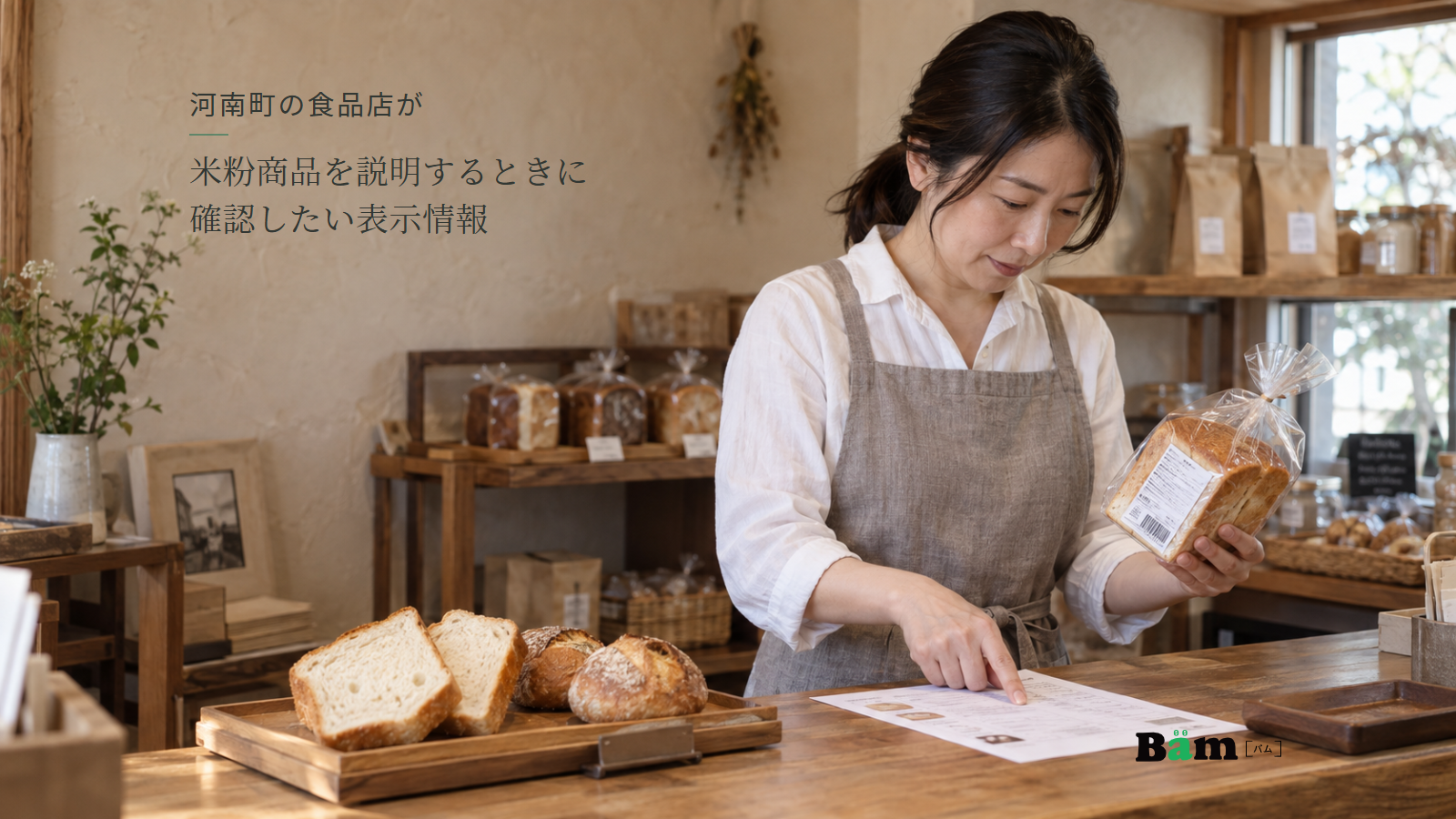 ベーカリーの店主が包装済み食パンの表示と紙の製造者資料を照合し、カウンターにパンの断面と丸パンが並ぶ場面、河南町の食品店が米粉商品を説明するときに確認したい表示情報の全文タイトル、右下のBämロゴ