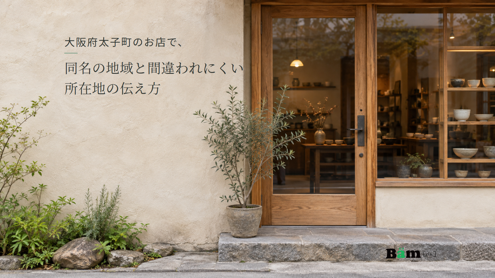 木枠の扉と器が見える窓、鉢植えのある小さなお店の入口。大阪府太子町のお店で、同名の地域と間違われにくい所在地の伝え方の全文タイトルと右下のBämロゴ