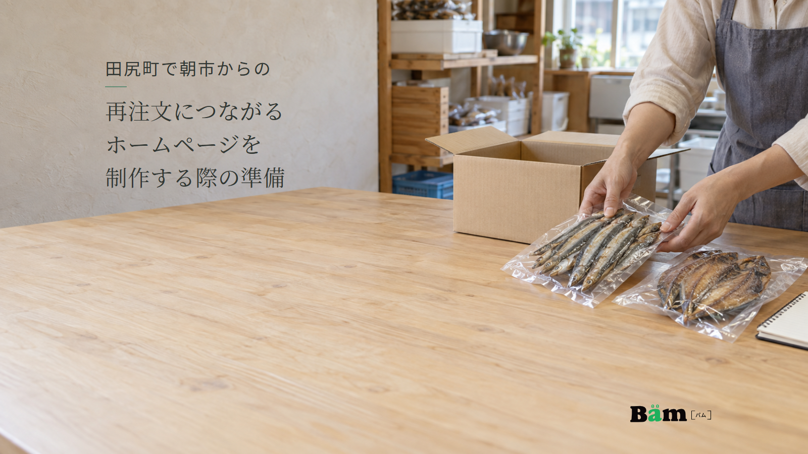 朝市で扱う干物の袋を、発送用の箱と見比べる店の作業台。田尻町で朝市からの再注文につながるホームページを制作する際の準備の全文タイトルと右下のBämロゴ