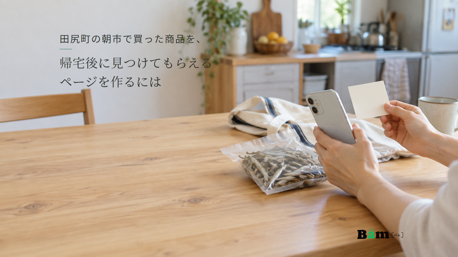 買ってきた干物の袋のそばで、小さなカードとスマートフォンを手に取る場面。田尻町の朝市で買った商品を、帰宅後に見つけてもらえるページを作るにはの全文タイトルと右下のBämロゴ